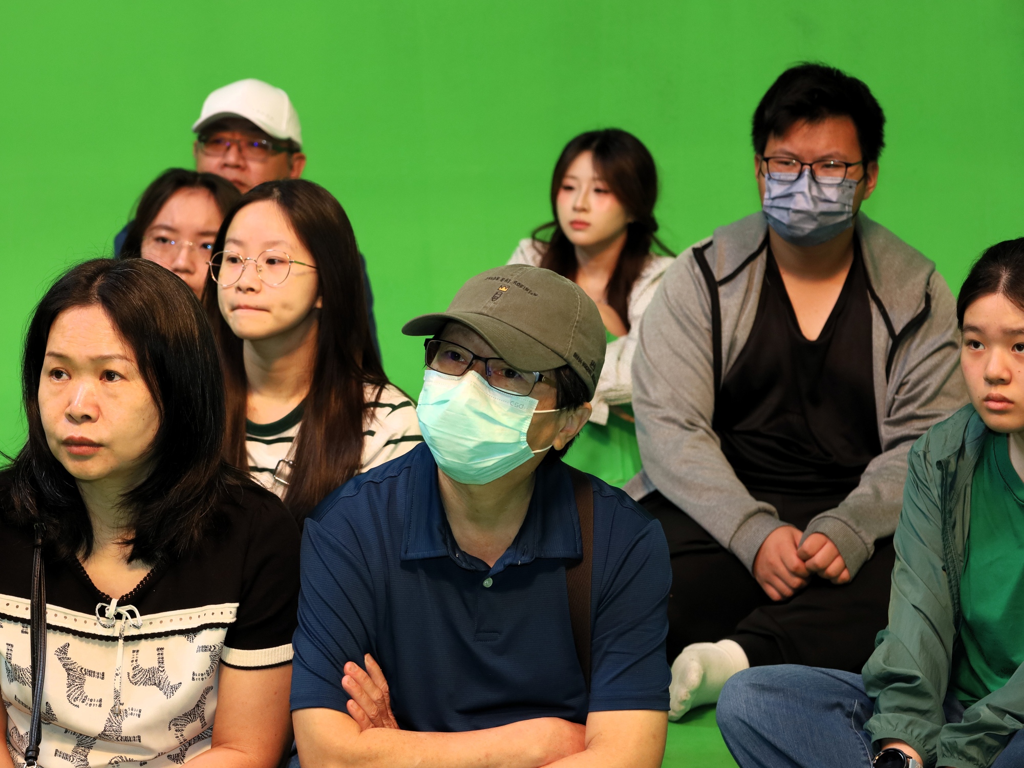 考生與家長戴著口罩，專注聽取資傳系AI綠幕攝影棚解說。